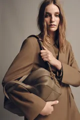 Bolso alargado tipo bowling color verde oliva, confeccionado en cuero con doble asa de mano y asa bandolera extraíble. Incluye bolsillo interior con cremallera y cierre principal con cremallera.