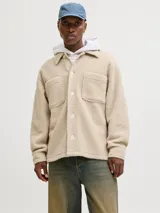 Sobrecamisa de textura teddy, color beige, con cuello camisero, cierre frontal de botones, mangas largas con puños abotonados y dos bolsillos frontales en el pecho.