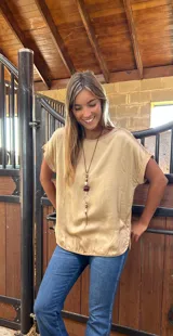 Blusa de satén color beige con cuello redondo, mangas cortas con dobladillo y corte holgado. La parte trasera está confeccionada en algodón con lycra para mayor comodidad y movilidad.