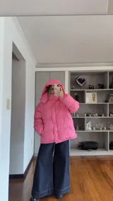 Campera puffer de corte holgado en color beige, con diseño acolchado, cuello alto y capucha desmontable. Cuenta con cierre frontal y botones a presión, además de puños elásticos.