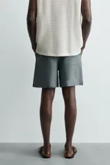 Bermuda de lino color blanco hueso, de corte relajado y tiro medio. Presenta cintura elástica ajustable con cordón, pliegues frontales y bolsillos laterales y trasero.