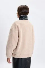 Campera de sherpa color crudo con detalles en cuero sintético negro en el cuello y la solapa frontal. Cuenta con cierre frontal y cuello alto con hebilla ajustable.