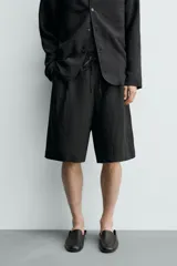 Bermuda relaxed fit de color negro, confeccionada en tejido fluido con viscosa y modal. Presenta cintura elástica ajustable con cordón, pliegues en el delantero, bolsillos frontales y bolsillos traseros de vivo.