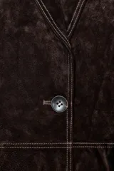 Blazer de piel 100% color marrón oscuro, con cuello solapa, manga larga con hombreras y bolsillos delanteros con solapa. Presenta pespuntes decorativos en contraste y cierre frontal con un botón.