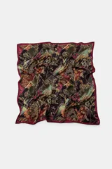 Pañuelo cuadrado de tejido satinado con estampado floral y botánico en tonos marrones, violetas y amarillos. Presenta un borde con línea a contraste.