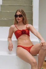 Conjunto de bikini color rojo óxido, compuesto por un top strapless con tirantes finos y detalle de flor textil en el centro, y una bombacha clásica de tiro medio.