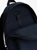 Mochila de poliéster color azul marino con ribetes negros. Presenta un diseño liso, asa superior, correas ajustables y acolchadas, y un panel trasero de malla acolchado. Cuenta con un compartimento principal amplio, funda para portátil incorporada, bolsillo interior con cremallera y bolsillo exterior con cremallera, donde se ubica el logo metálico de Tommy Hilfiger.
