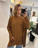 Sweater de tejido de punto con diseño de ochos, color beige, de corte holgado y manga larga con puños ajustados. Presenta dos bolsillos frontales tipo parche con detalle de etiqueta de cuero.