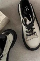 Botas de cuero color beige con suela track negra de goma y cordones gruesos negros. Presentan un diseño de caña baja con costuras visibles y puntera reforzada.