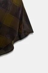 Top de cuello halter con espalda descubierta, confeccionado en tejido de viscosa con estampado de cuadros en tonos verde oliva y negro. Presenta un diseño asimétrico en el bajo y cierre con botones en la parte posterior del cuello.