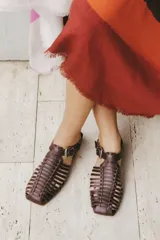 Sandalias planas tipo huarache de cuero negro, con tiras entrelazadas a mano y tira ajustable en el talón con hebilla metálica.