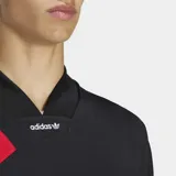 Remera Adidas de estilo futbolístico inspirada en los años 90, color negro con cuello en pico y tres bandas diagonales rojas sobre el hombro derecho. Presenta un corte holgado y logo de la marca en el centro del cuello.