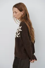 Buzo de tejido de punto en color beige, con cuello redondo y mangas largas. Presenta un delicado bordado de ramas y hojas en color crema en la parte superior del frente.