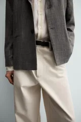 Pantalón chino de corte relajado, confeccionado en tejido estructurado de color beige. Presenta bolsillos frontales, bolsillos traseros de vivo y cierre frontal con cremallera y botón.