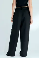 Pantalón sastrero negro de corte holgado, con diseño cruzado asimétrico en el frente, pinzas y piernas amplias.