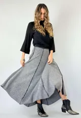 Pollera larga tejida de lana, con diseño de rayas verticales en tonos grises y negros, y paneles lisos en gris claro. Presenta un corte asimétrico y aberturas laterales.