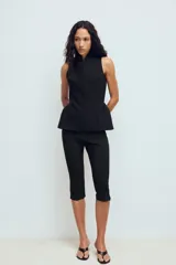Chaleco entallado de color negro con cuello alto y cierre frontal con cremallera oculta. Presenta un diseño sin mangas con costuras verticales que definen la silueta y un bajo con ligero volumen acampanado.