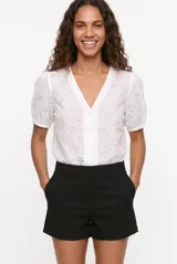 Blusa blanca de broderie con escote en V y cierre frontal de botones, mangas cortas abullonadas.