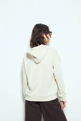 Canguro negro de calce relajado con capucha y cordones ajustables. Presenta un estampado gráfico frontal de un ojo con rayos de sol y la frase "STAY WEIRD".