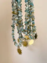 Collar tipo gargantilla compuesto por piedras naturales en tonos celestes y verdes con separadores dorados, presenta un dije central grande en forma de sol de metal dorado.