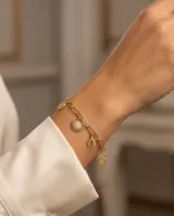 Pulsera de cadena de eslabones dorada con cinco dijes colgantes decorados con circonias: un corazón, una mano de Hamsa, un sol, un hueso de la suerte y un círculo.