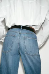 Jeans de tiro alto con pernera ancha y corte cropped. Presenta diseño de cinco bolsillos, cierre frontal con cremallera y botón, e incluye un cinturón oscuro con hebilla metálica.