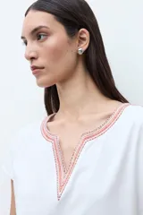 Remera blanca de algodón con escote en V y detalles de bordado étnico en tonos rojizos y naranjas en el cuello y los hombros. De corte recto y manga corta.