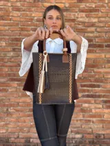 Bolso matero de cuero color chocolate con textura croco, asas cortas y detalle de costuras en los laterales. Incluye un dije con flecos en tonos beige y negro.