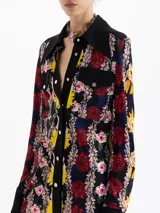 Camisa de manga larga con estampado floral sobre fondo negro. Presenta cuello, cartera de botones, puños y canesú en color negro liso. Tiene dos bolsillos plaqué con tapa en el frente, asegurados con broches metálicos negros grabados.