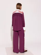 Pantalón sastrero largo color borgoña con recortes a contra tono y estampado floral en el delantero. En ambos laterales lleva flecos de tela base al tono.