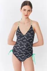 Malla enteriza negra con estampado de hongos blancos, escote en V, tirantes finos color verde neón y laterales ajustables con cordones del mismo color.