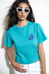 Remera turquesa de algodón con cuello redondo y mangas cortas abullonadas. Presenta un bordado en el pecho con forma de animal.