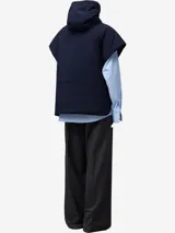 Chaleco acolchado de color azul marino, con capucha ajustable mediante cordón y cierre frontal de cremallera. Presenta bolsillos de vivo inclinados en el delantero y cierres laterales con broches a presión.