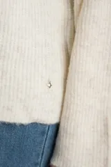 Sweater de tejido de punto color blanco roto o crema, con textura jaspeada. Presenta cuello polo y un escote con tres botones nacarados. El calce es holgado (oversize) y tiene mangas largas.