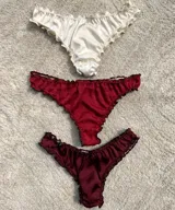 Pack de tres bombachas de satén con volados de encaje. Incluye una bombacha color crema, una color rojo y una color borgoña.