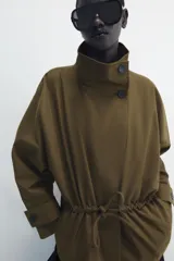 Parka amplia de Zara Woman Collection confeccionada en hilatura con mezcla de algodón, en color verde militar. Presenta cuello alto, manga larga con trabillas y botón, bolsillos laterales ocultos en costura, cintura ajustable con cordones y cierre frontal con botones.