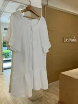 Vestido blanco de lino con escote con lazo, mangas cortas amplias con volados y ruedo con volados.