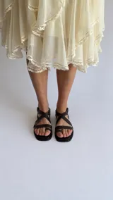Sandalias de cuero color marrón con diseño de tiras cruzadas en el empeine, sujetador para el dedo y tira ajustable con hebilla en el talón.