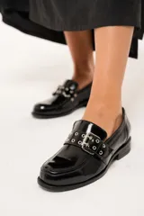 Mocasines negros de charol arrugado con horma redondeada y detalle de presilla con hebilla y ojalillos.