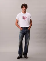 Remera Calvin Klein de corte relajado, confeccionada en algodón grueso blanco. Cuenta con cuello tipo mock y logo estampado en el pecho con tipografía cursiva en tono bordó.