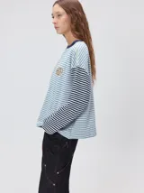 Remera de manga larga con diseño a rayas horizontales en tonos celestes y blancos en el cuerpo, y mangas a rayas azul marino y blancas. Presenta cuello redondo en color azul marino, logo bordado en el pecho y calce holgado.