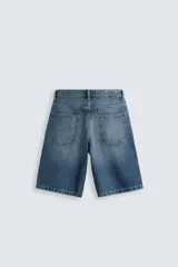 Bermuda de denim de algodón, color azul medio lavado, de corte ancho (baggy fit) y largo hasta la rodilla. Presenta cinco bolsillos y cierre frontal con cremallera y botón.