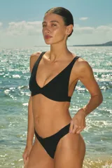 Conjunto de bikini negro de lycra texturada, compuesto por un corpiño triangular fijo con elástico interno bajo el busto y una bombacha vedetina con elástico interno.