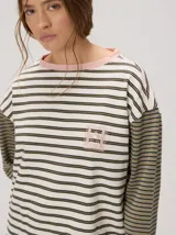 Remera manga larga de corte oversize y cuello redondo, con diseño a rayas horizontales en tonos claros y verde militar, y detalle de bordado frontal.