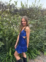 Vestido corto color bordó con escote en V, diseño de top triangular y aberturas laterales en la cintura. Presenta breteles finos cruzados en la espalda y falda con doble volado irregular en el ruedo.
