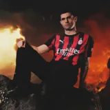 Camiseta de fútbol Puma del AC Milan, modelo Home. Diseño clásico a rayas verticales rojas y negras, con cuello redondo negro y logo de la marca y escudo del club en el frente.