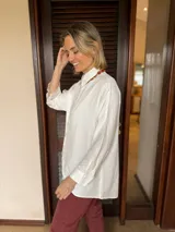 Camisa de corte clásico y calce holgado, color blanco, con cuello camisero, cierre frontal de botones ocultos y mangas largas con puños abotonados.