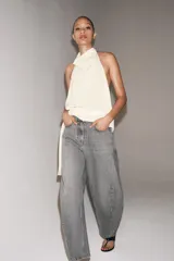 Jeans de tiro medio con diseño de pierna tipo balloon y largo al tobillo. Presenta cinco bolsillos, cierre frontal con cremallera y botón, y un acabado con efecto lavado.