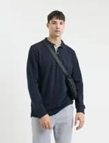 Remera de manga larga con cuello polo, confeccionada en tejido de punto canalé francés. Presenta abotonadura frontal con botones de madera y detalles a contratono en la cartera y el interior del cuello.