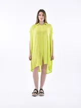 Vestido camisero de corte holgado y diseño asimétrico, con cuello clásico, cierre frontal de botones y mangas cortas con terminación caída.